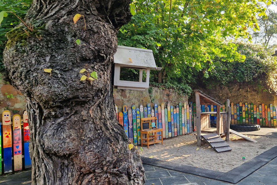 Außenbereich mit Baum, Vogelkasten, Sandkasten, angemalten Zaunslatten